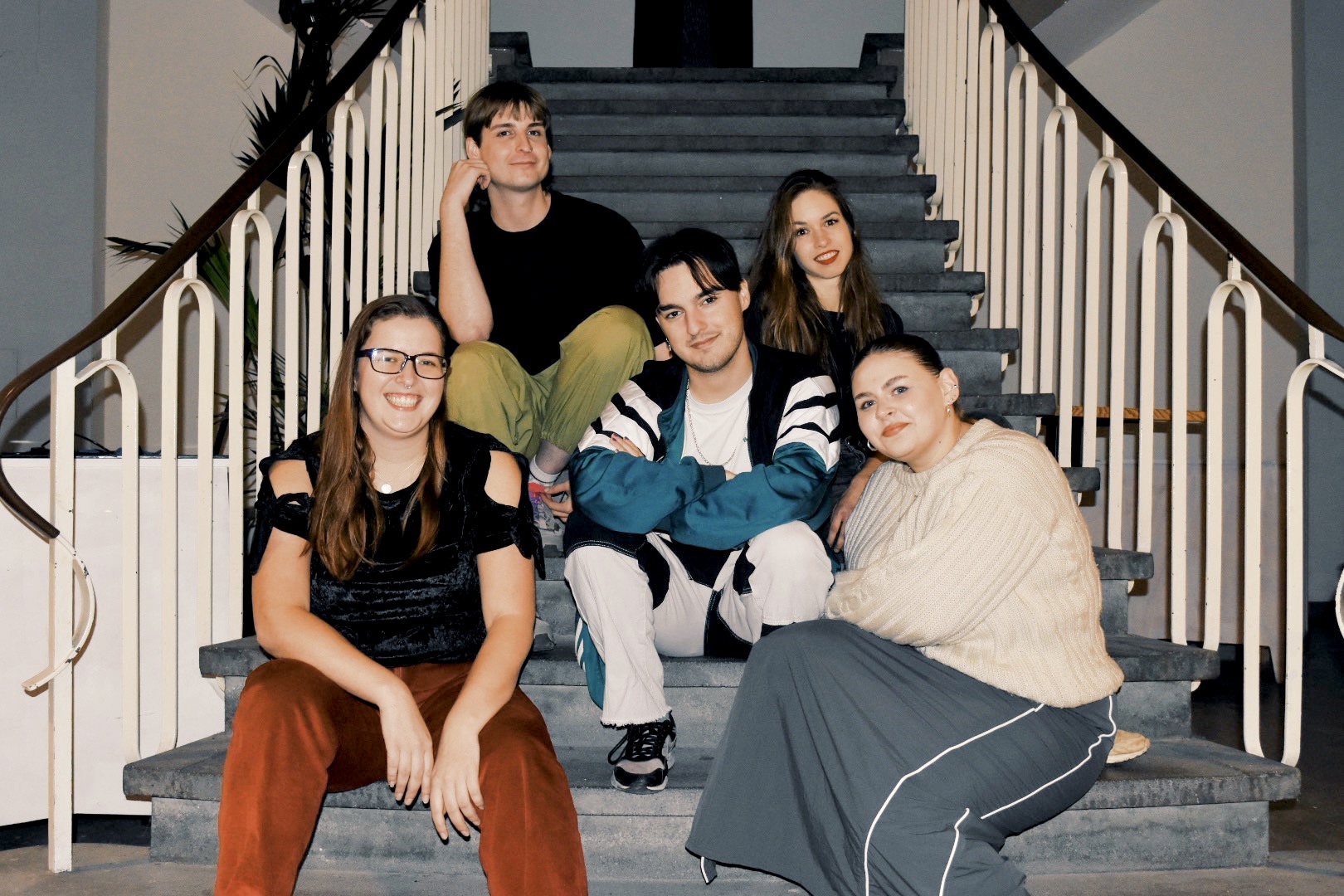 De crew van Queerapie zit lachend op een trap